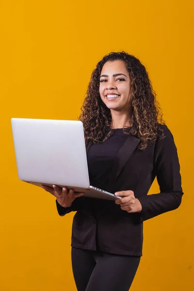 Portrait of young woman in executive outfit with laptop on yellow background. Businesswoman working with laptop. Vertical