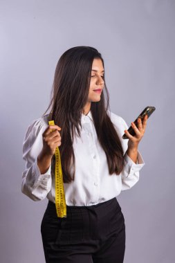 Brezilyalı kadın, beslenme uzmanı, elinde mezura ve akıllı telefon var..