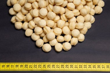 wheat, heap of round wheat snacks next to measuring tape, black background clipart