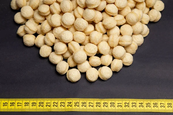 stock image wheat, heap of round wheat snacks next to measuring tape, black background