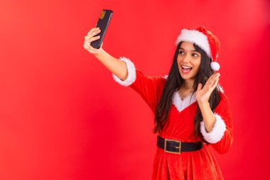 Brezilyalı genç bir kadın Noel kıyafetleri giyiyor, akıllı telefondan selfie çekiyor..