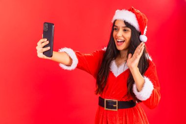 Brezilyalı genç bir kadın Noel kıyafetleri giyiyor, akıllı telefondan selfie çekiyor..