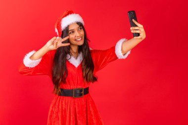 Brezilyalı genç bir kadın Noel kıyafetleri giyiyor, akıllı telefondan selfie çekiyor..