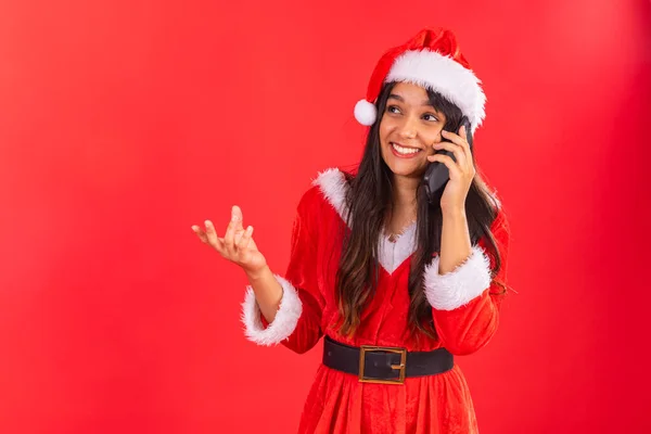 Brazilian teenage woman wearing Christmas clothes, smartphone on voice call.