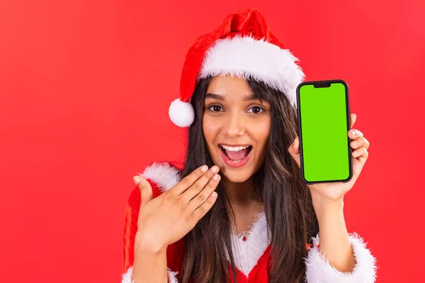 Brazilian teenage woman, wearing Christmas clothes, showing smartphone with green screen in chroma key, mobile advertisement, app.