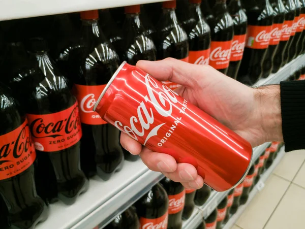 Zaporizhzhia, Ukrayna - 23 Mayıs 2022: Bir adamın elinde kırmızı bir Coca-Cola kutusu ile bir Coca-Cola şişesinin arka planında