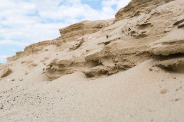 Mavi bulutlu gökyüzüne karşı rüzgarın erozyonuyla oluşan kum formları.
