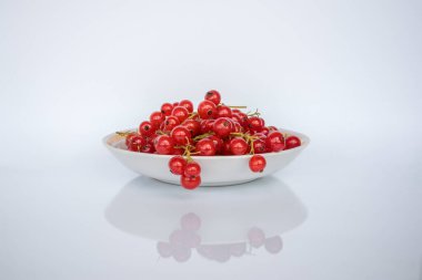 Red currant berries in a saucer on a white background with reflection