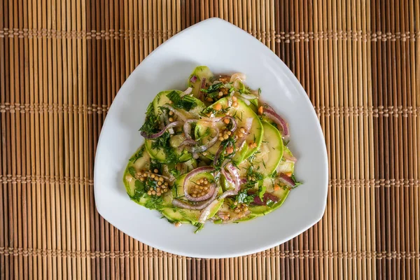 Marinated zucchini in lemon sauce with onion and mustard seeds on a bamboo tablecloth top view
