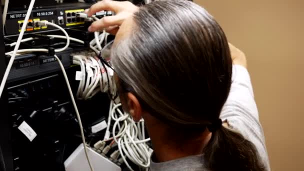 メガネ付きの中年エンジニアとサーバールーム内のポニーテールがサーバールーム内のネットワークケーブルを接続 — ストック動画