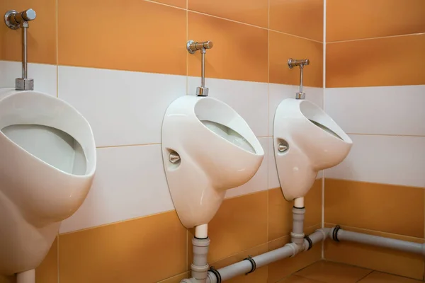 室内卫生间 墙壁上有白色和橙色瓷砖 公共卫生间里有一排装有男厕的卫生用品 — 图库照片