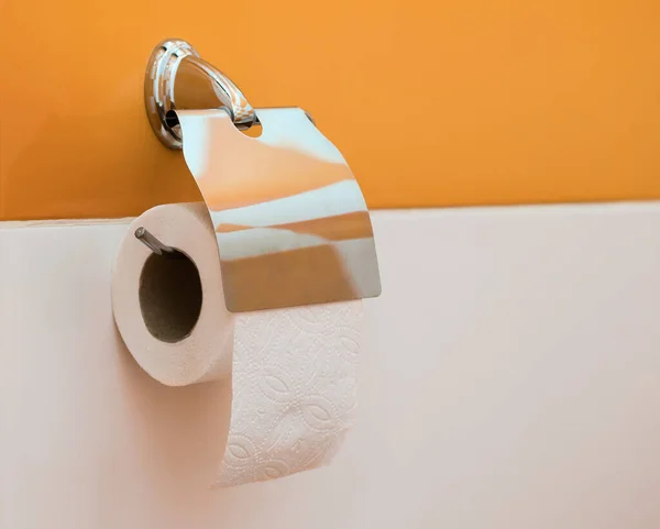 在厕所的橙色和白色墙壁上有一卷卫生纸的不锈钢笔架 — 图库照片