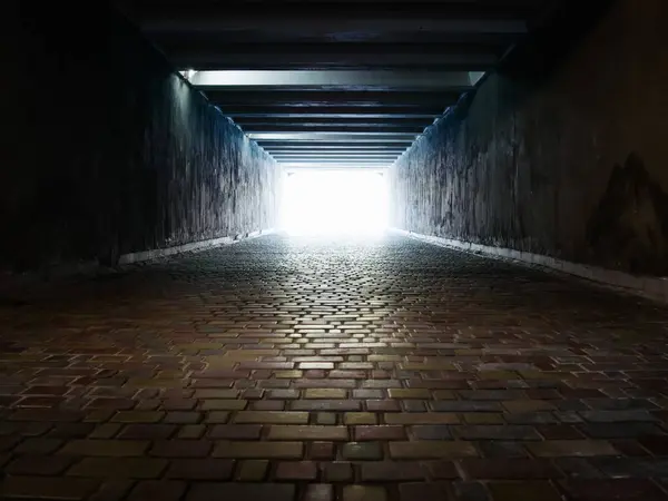 Çok renkli kaldırım taşlarıyla döşenmiş karanlık bir yaya tünelinin sonundaki ışık. Arkaplan