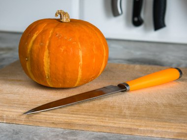 Dikdörtgen kayın üzerinde balkabağı kesme tahtası ve turuncu saplı bir bıçak.