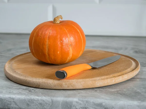 Pumpkin on a round beech cutting board and a knife with an orange handle