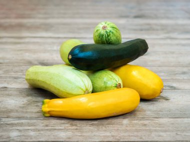 Boyanmamış ahşap bir masada taze sarı ve yeşil kabak.