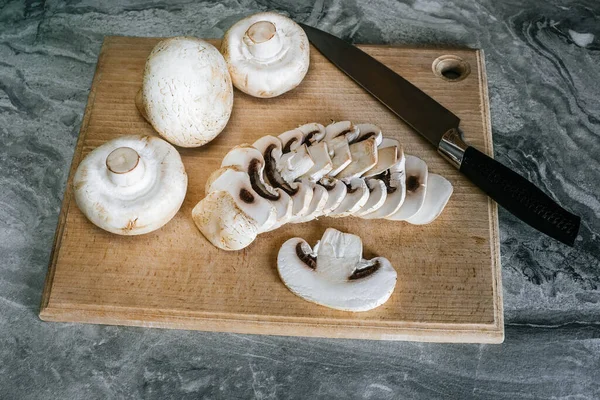 Kayın kesme tahtasındaki şampiyon mantarların en üst görüntüsü. Bir tanesi bıçakla kesilmiş.