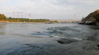 Kayalar ve akıntılar arasında bir köprünün ve yüksek voltajlı elektrik hatlarının zeminine karşı geniş bir nehrin hızlı akışı