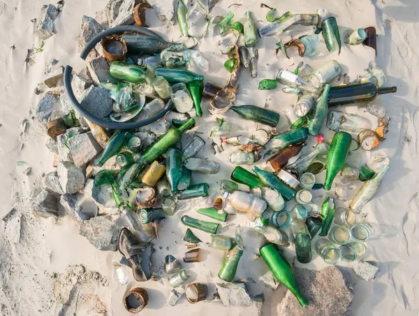 Çoğu eski şişeler ve kırık camlar olan kumun üzerindeki büyük bir çöp yığını manzarası. Arkaplan