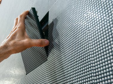 Bir adamın eli, tamir ve bakım sonrası büyük bir LED ekranın yüzeyindeki yerinden kare bir LED modülü kuruyor..