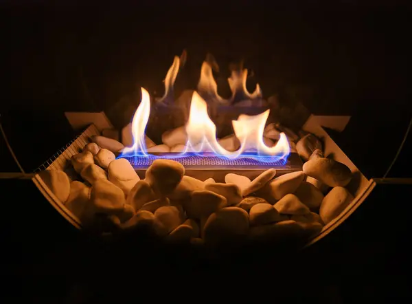 Beyaz taşları ve cam panelleri olan dekoratif bir şöminede alevler.