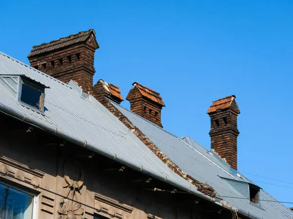 Güneşli bir günde mavi bulutsuz gökyüzünün arka planına karşı bir evin çatısındaki antik tuğla bacalar.