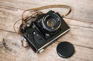 Zaporizhzhia, Ukrayna - 4 Ağustos 2024: Siyah Sovyet film kamerası ZENIT TTL ahşap boyanmamış bir yüzey üzerinde düğümlerle kaplı deri bir çantada