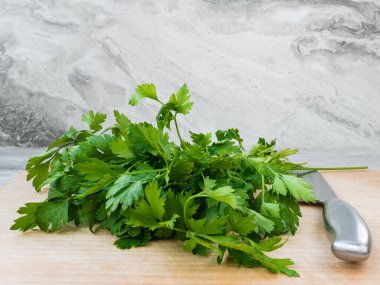 Kesme tahtasının üzerinde bir demet taze maydanoz ve paslanmaz saplı bir bıçak..