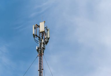 Mavi gökyüzüne karşı hareketli hücresel antenleri olan uzun bir direğin tepesi