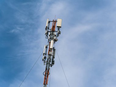 Mavi gökyüzüne karşı hareketli hücre antenleri olan uzun bir direğin alt görüntüsü