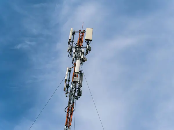 Mavi gökyüzüne karşı hareketli hücre antenleri olan uzun bir direğin alt görüntüsü