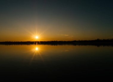 Ormanlık kıyıları olan geniş bir nehrin üzerinde turuncu, canlı bir gün batımı. Arkaplan