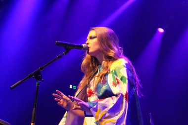 Genç bir kadın sahnede mikrofonla şarkı söylüyor.