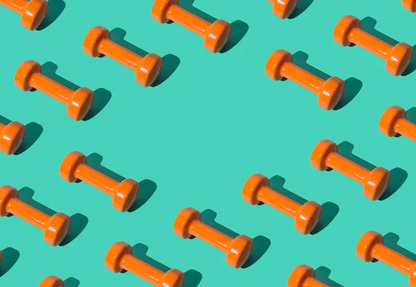 Creative pattern composition made of orange dumbbells on pastel green background with copy space. Minimal fitness, healthy lifestyle and sport concept. Trendy exercise and fitness backround idea.