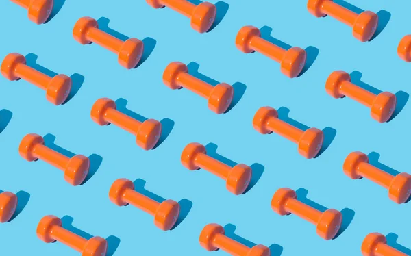 Creative pattern composition made of orange dumbbells on light blue background. Minimal fitness, healthy lifestyle and sport concept. Trendy exercise and fitness backround idea.