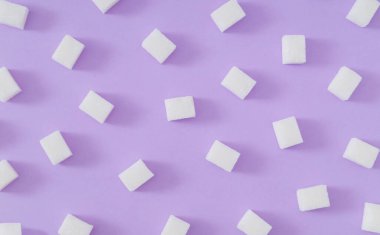 Pastel menekşe arkaplanındaki şeker küplerinden oluşan yaratıcı desen. Minimum gıda konsepti. Moda düz zemin arka plan kompozisyonu. Süslü küp şeker fikri. Üst görünüm.