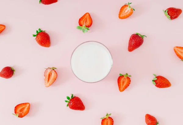 Creative pattern composition made of milk drink with strawberry taste in glass cup and red strawberries on pastel pink background. Minimal smoothie or milkshake concept. Healthy food for breakfast.