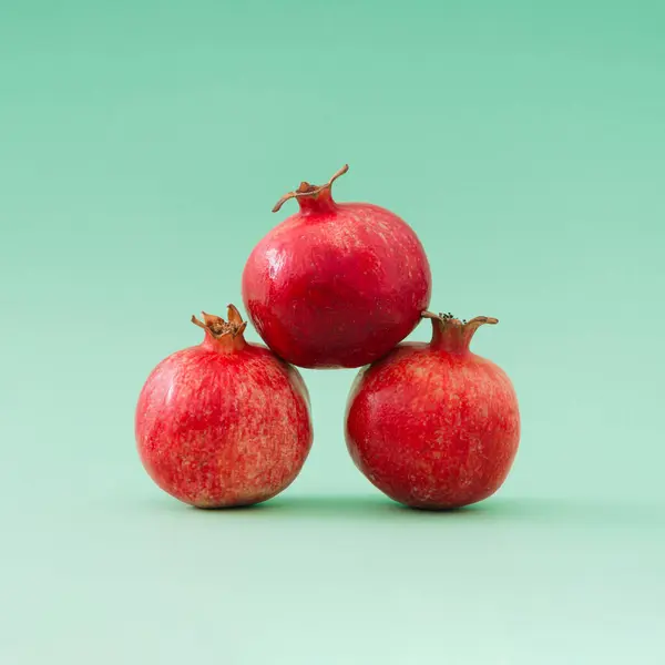Keep the balance. Creative arrangement of red pomegranates against pastel green background. Minimal natural fruit concept. Trendy healthy food idea. Pomegranate aesthetic background.