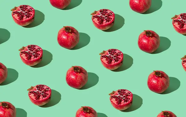 Trendy fruit pattern made of fresh red pomegranates on light pastel green background. Minimal healthy food layout. Nature fruit concept. Pomegranate aesthetic background pattern.