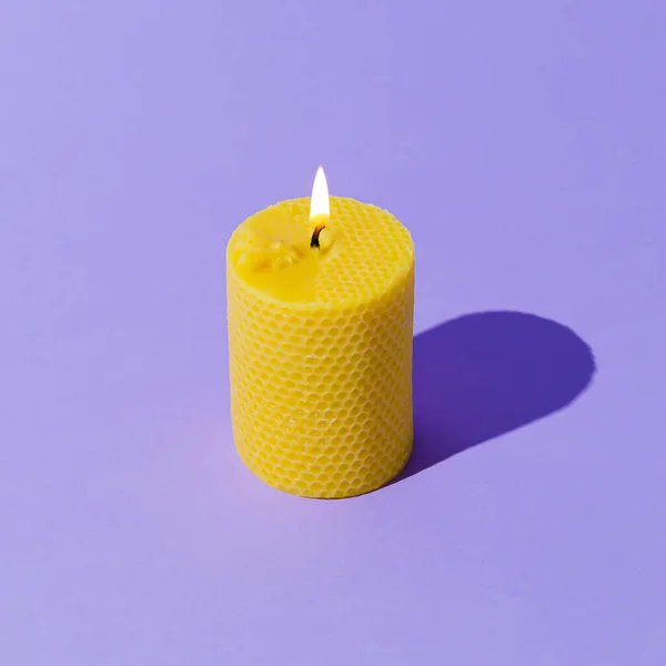 Creative layout of beeswax candle made with natural wax produced by honey bees on pastel violet background. Minimal concept. Trendy beeswax candle composition.