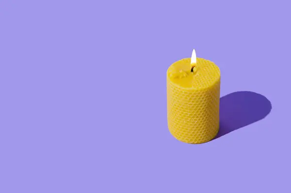 Creative layout of beeswax candle made with natural wax produced by honey bees on pastel violet background. Minimal concept. Trendy beeswax candle composition. Copy space.