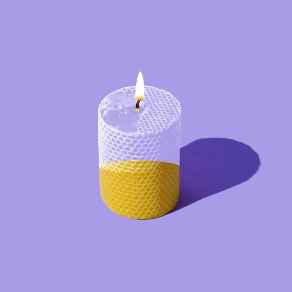 Creative layout of beeswax candle made with natural wax produced by honey bees on pastel violet background. Minimal concept. Trendy beeswax candle composition.