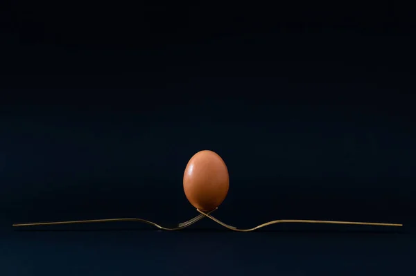 Keep the balance. Creative composition made with egg and golden forks on black background. Minimal food concept. Trendy egg and forks idea. Food aesthetic.