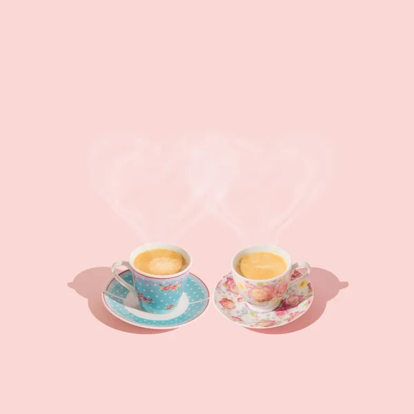 Creative layout with love hearts made of steaming coffee. Pink and blue cups of coffee on light pastel peachy pink background. Minimal love concept. Coffee aesthetic. Trendy coffee with love idea.