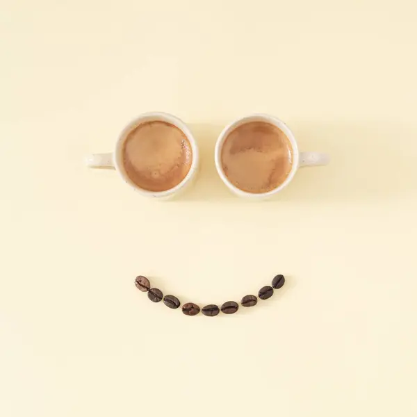 Layout of smiley emoticon made with coffee cups and coffee beans on pastel background. Minimal coffee concept. Creative positive thinking and good mood idea composition. Coffee aesthetic. Flat lay.