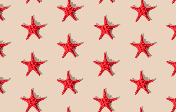 Summer pattern composition made with red starfish on sandy color background. Minimal summer concept. Creative sea star flat lay pattern idea. Top of view.