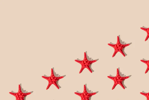 Summer pattern composition made with red starfish on sandy color background. Minimal summer concept. Creative sea star flat lay pattern idea. Top of view. Copy space.