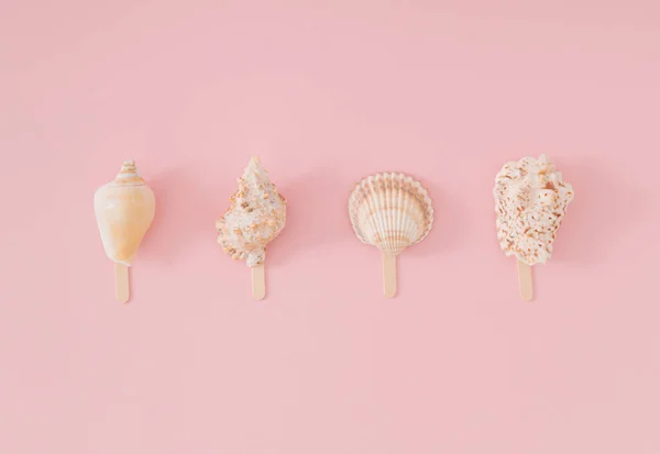 Trendy summer layout of sea shells with ice cream stick on light peachy pink background. Minimal summer concept. Creative beach food idea. Ice cream aesthetic. Flat lay. Top of view.