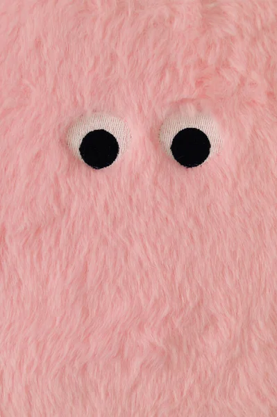 Cute fluffy monster made with pastel pink faux fur. Minimal concept. Creative funny face composition. An original peachy pink fur background image idea. Flat lay, top of view.