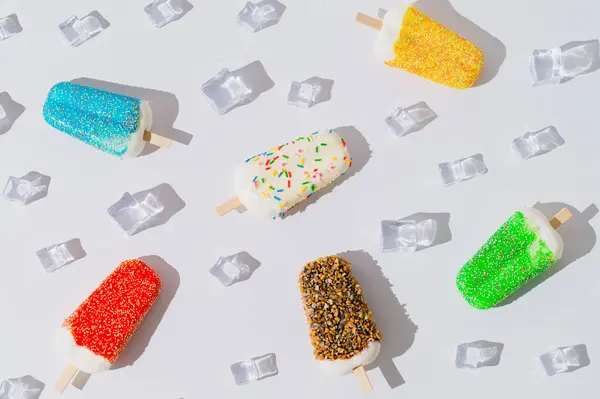 Summer pattern composition made with colorful ice cream popsicles and ice cubes on white background. Minimal creative summer concept. Trendy summertime sweet food layout. Flat lay.